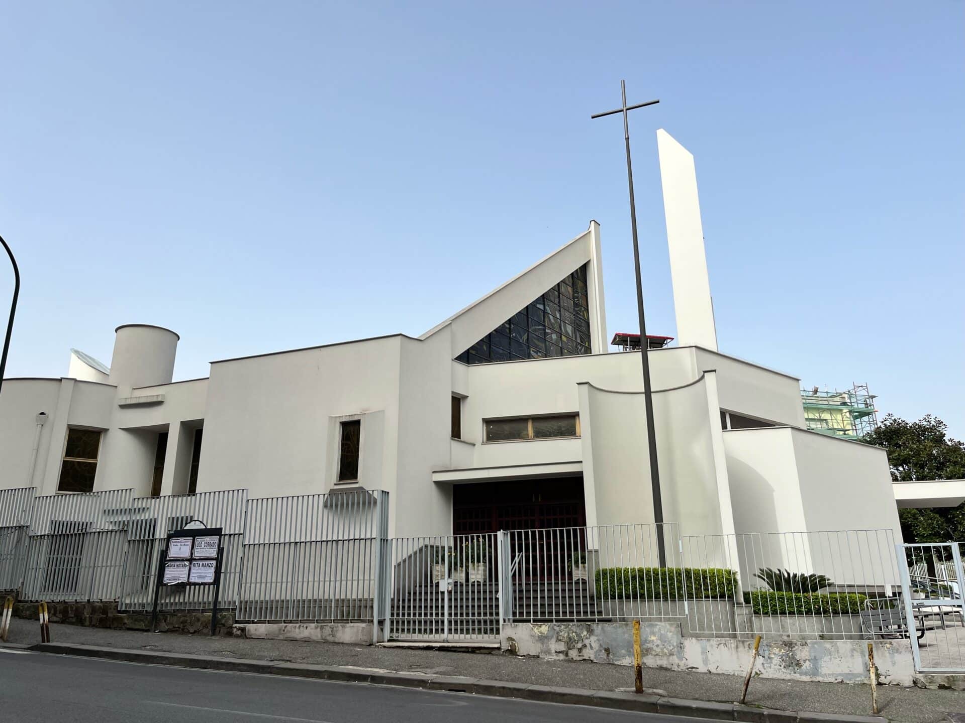 Chiesa moderna con croce esterna e cielo azzurro.