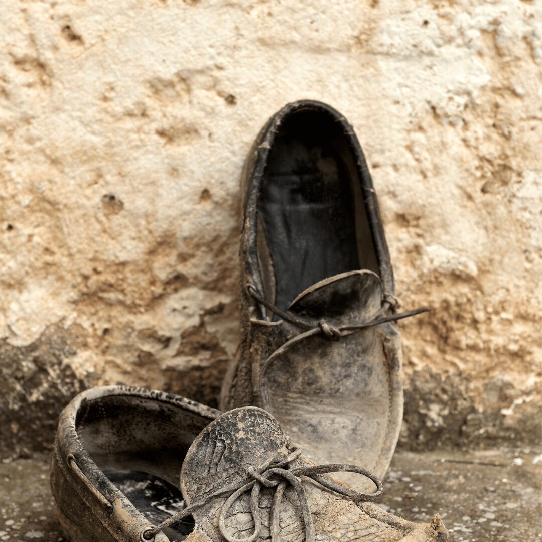 Vecchie scarpe consumate su muro di pietra.