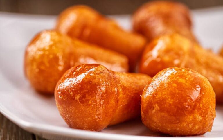 Zeppole dorate e zuccherate su piatto bianco.