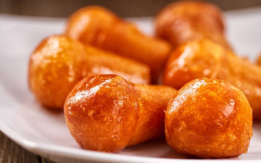 Zeppole dorate e zuccherate su piatto bianco.